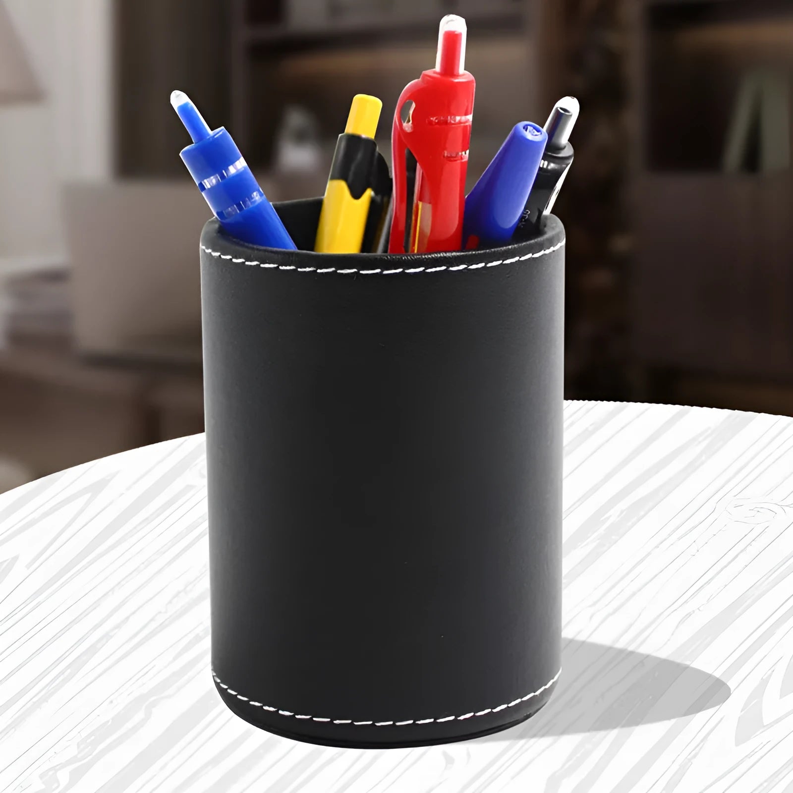 Round black leather pen container on desk holding writing instruments