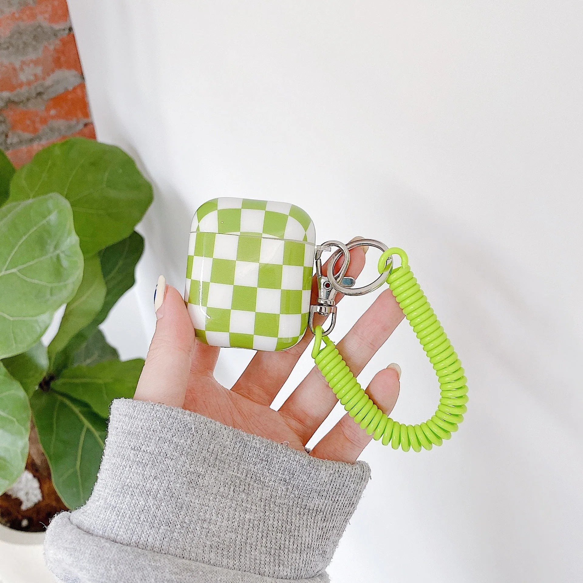 Black and green checkerboard pattern TPU protective case covers for Apple AirPods, one with a smiley face lanyard.