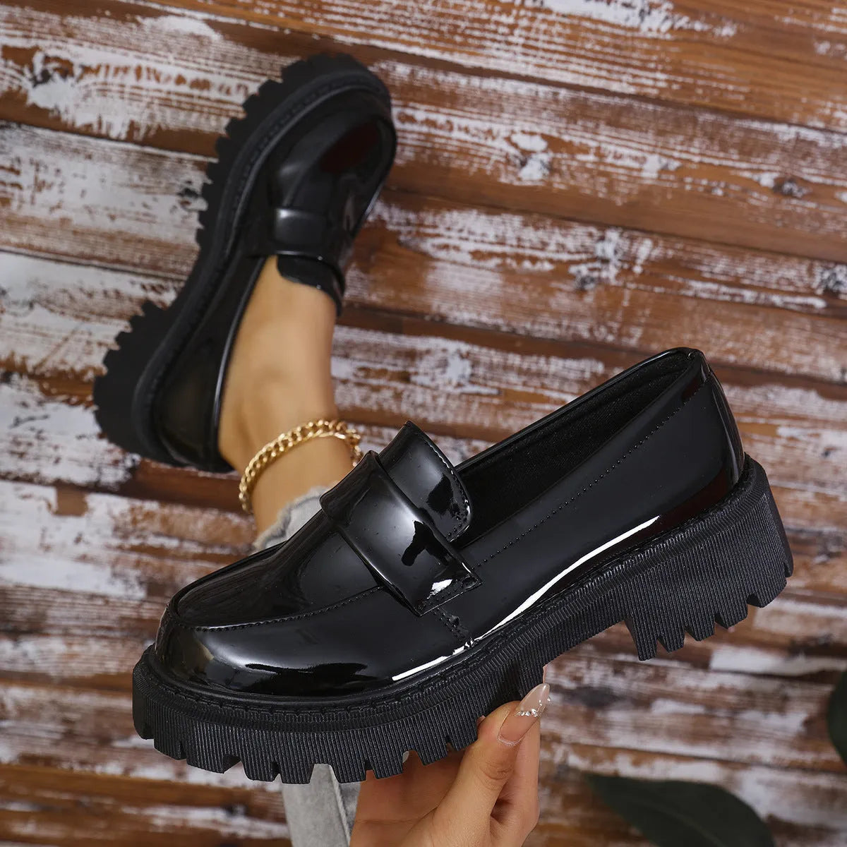 Black slip-on loafers with a chunky platform heel and thick rubber sole on a wooden floor.