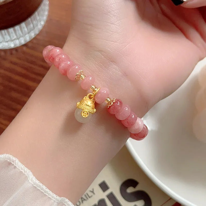 Women's lucky cat bracelet made from strung strawberry quartz or grey jade stones with zodiac charms.