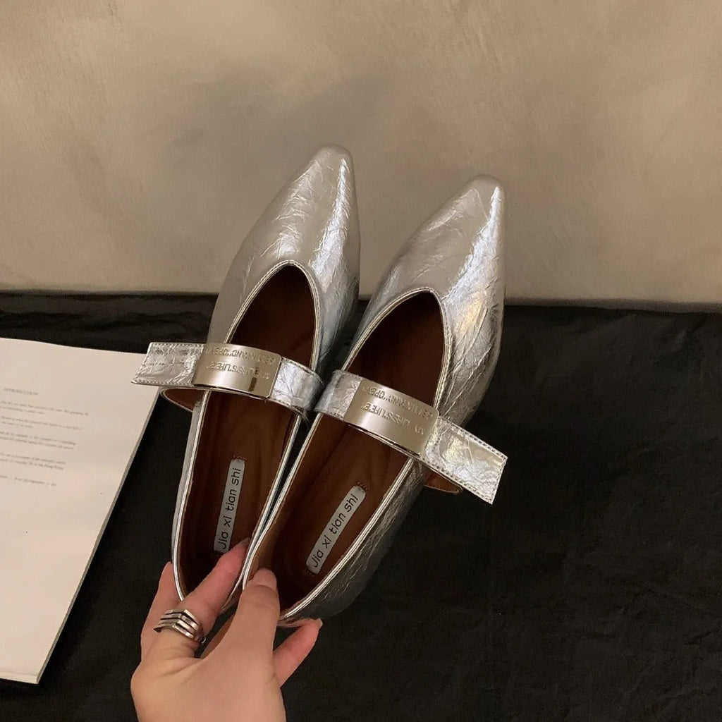 Women's black pointed toe Mary Jane shoes with a silver buckle on a low flat heel.