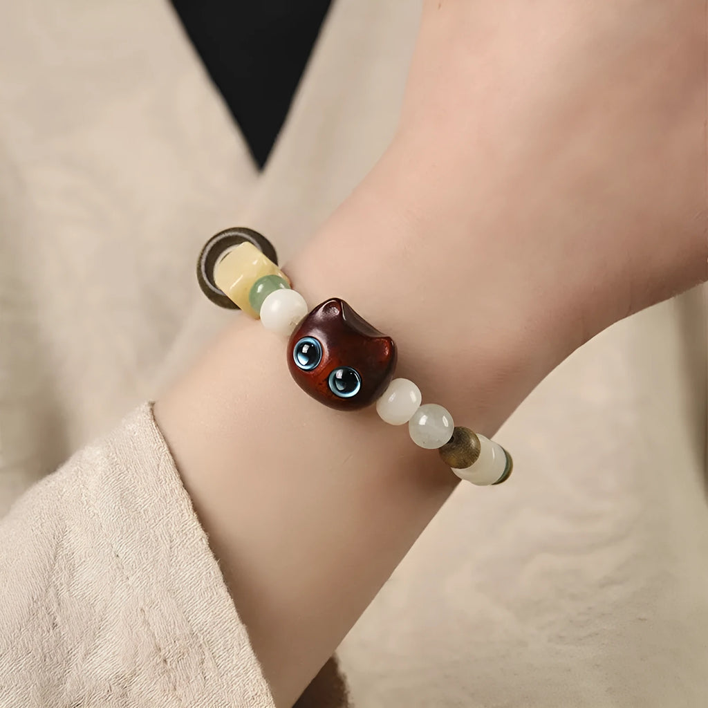 Hand-woven Buddhist bracelet with jade beads, wood elements, and cat's paw charm in rosewood or ebony with yellow or blue eyes