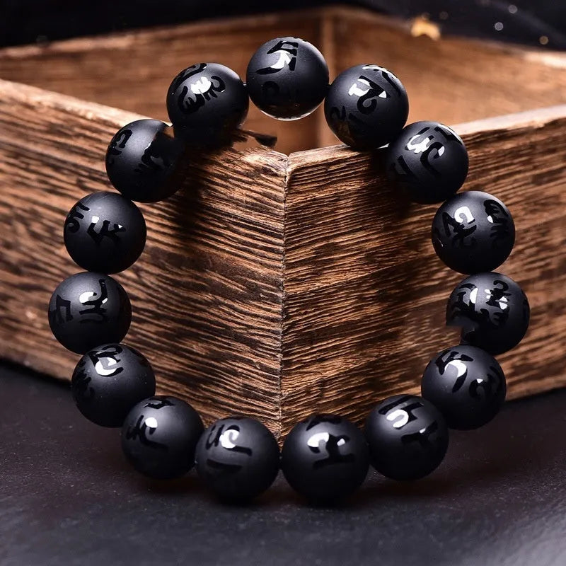 Close-up of a frosted black agate bracelet showing engraved Sanskrit mantra and Chinese-style patterns on a stone bead.