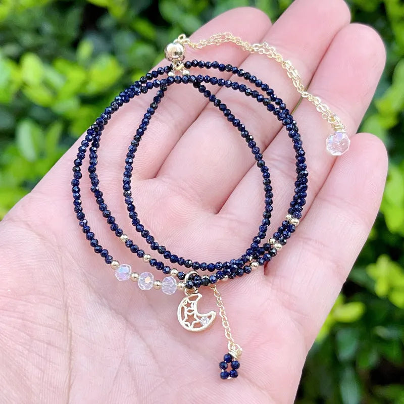 Close-up of a women's multi-layer bracelet with three blue gold sand stone rings on a wrist.