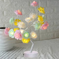 White and red rose shaped LED table lamp with bonsai tree base on a wooden table.
