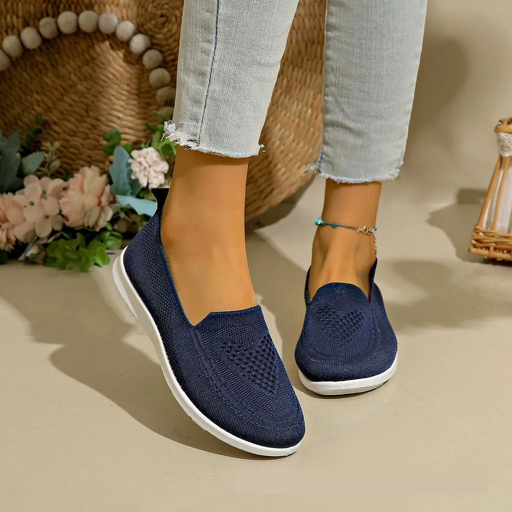 Women's beige canvas slip-on shoe with heart-shaped perforations and a flat sole.