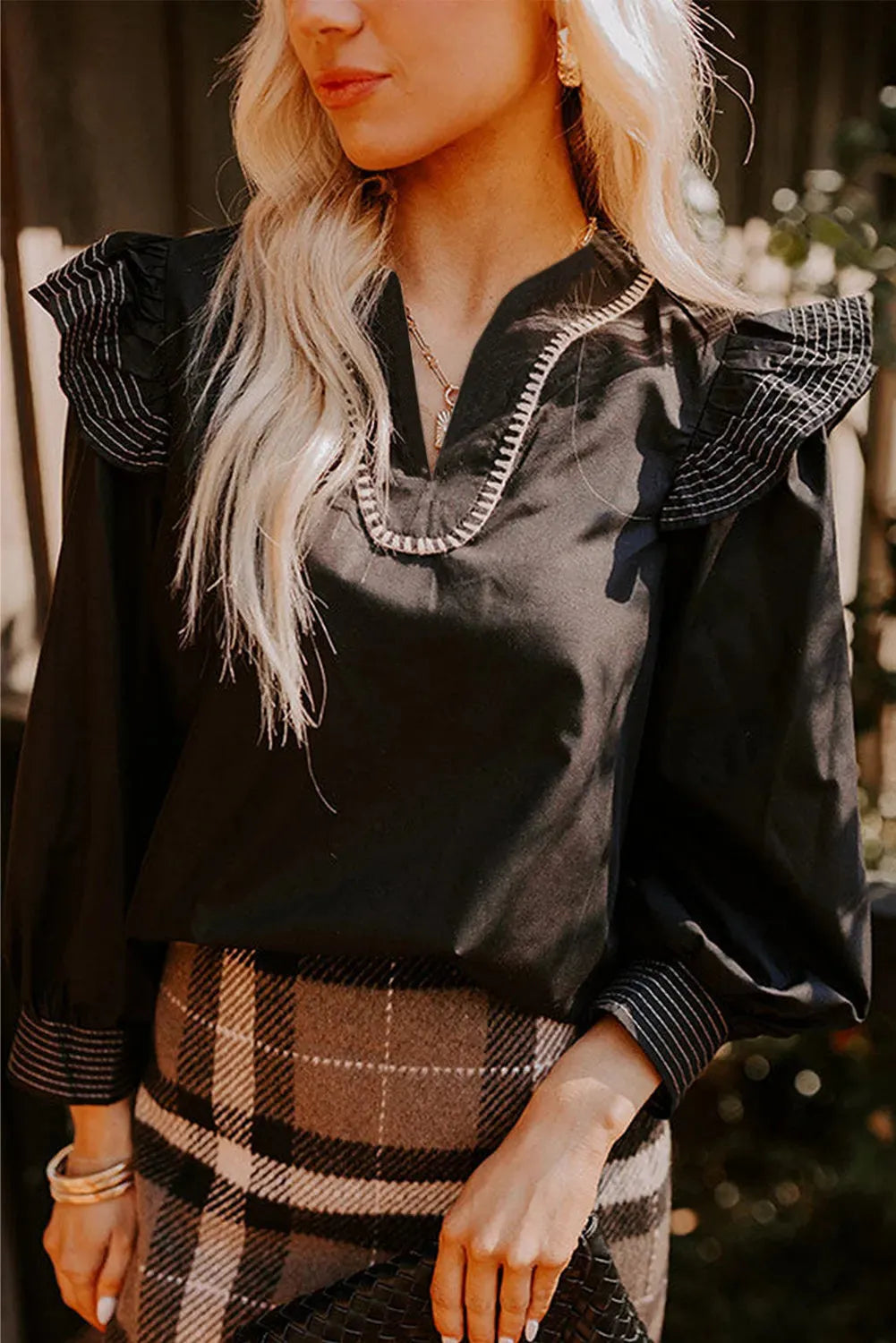 Black women's V-neck blouse with contrast stitching on the neckline and long sleeves with a ruffle detail.