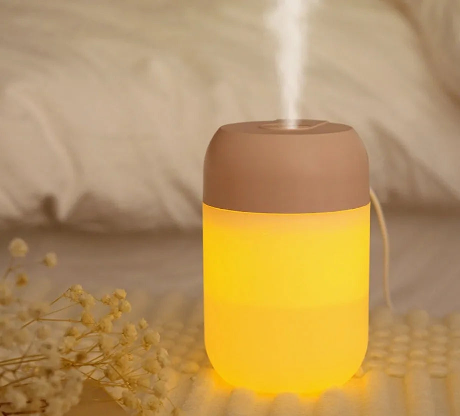 Small white cylindrical USB-powered humidifier with charging cable on a desk.