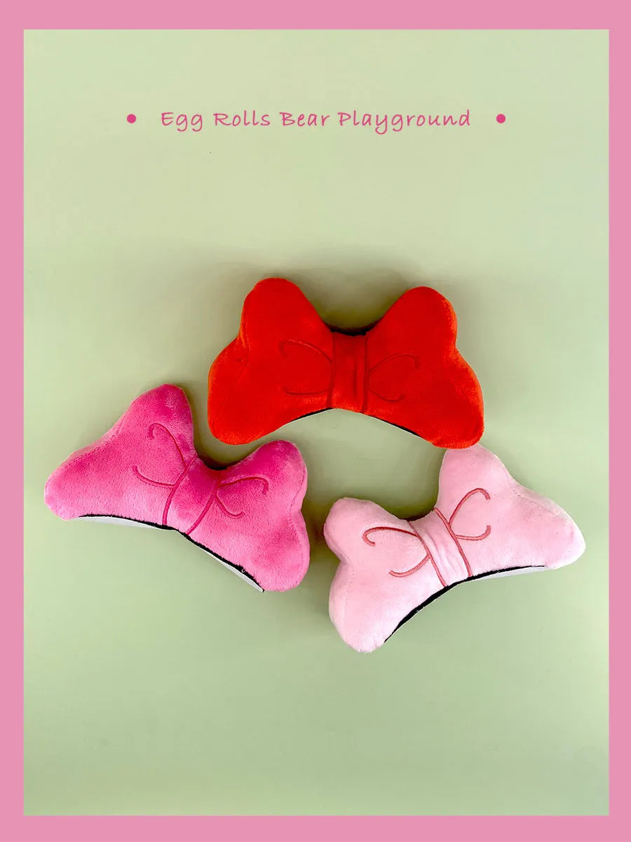 A soft red plush bow tie decoration for attaching to a motorcycle or ski helmet.