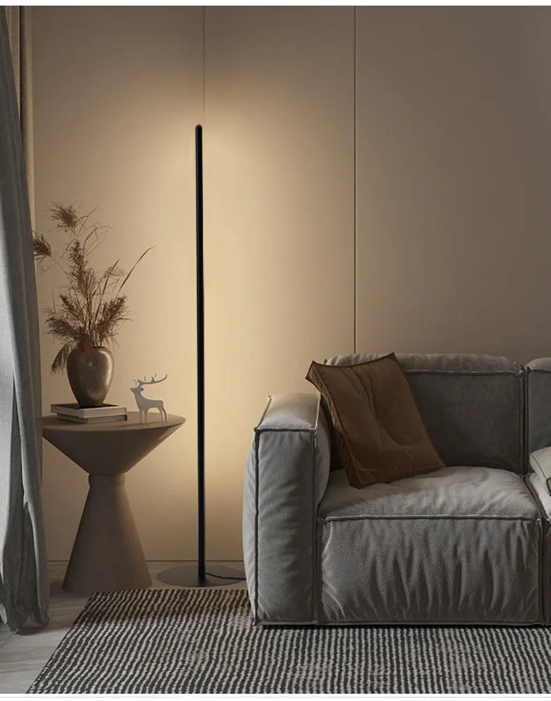 Modern vertical aluminium alloy floor lamp in silver, shown beside a sofa in a living room setting.