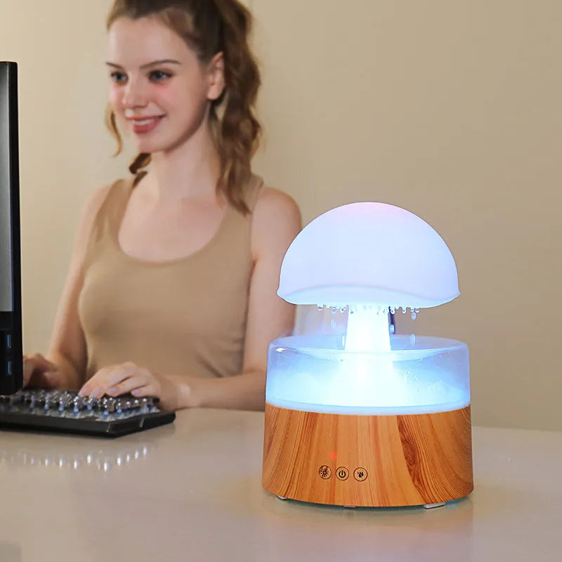White cloud-shaped humidifier with raindrop simulation and colour-changing lights on wooden surface