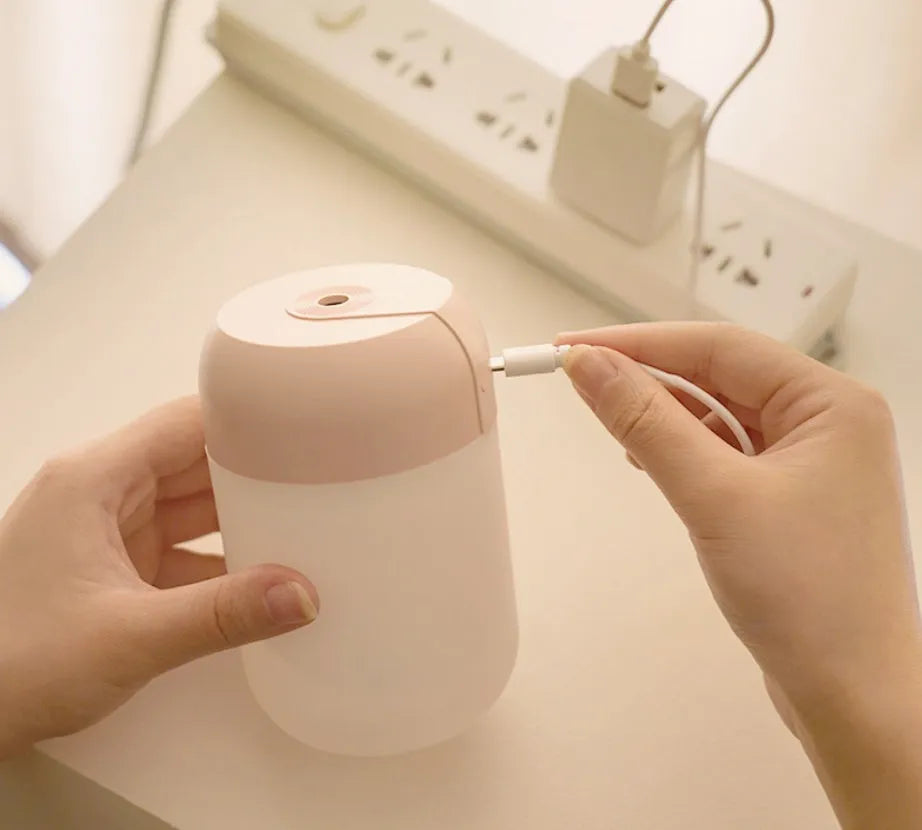 Small white cylindrical USB-powered humidifier with charging cable on a desk.