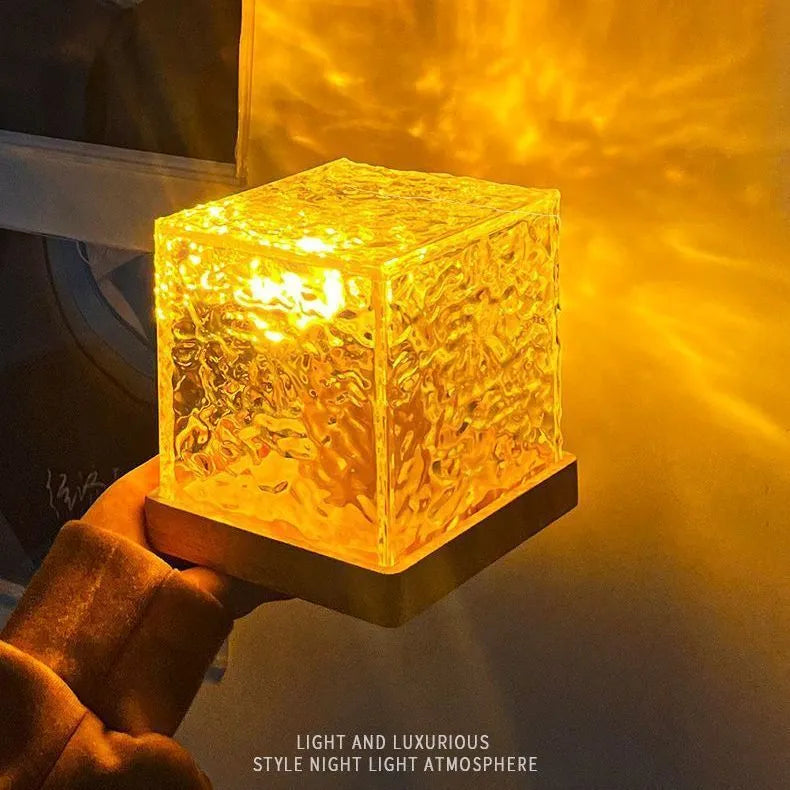 Modern geometric crystal table lamp projecting colourful water ripple light effect on wall.