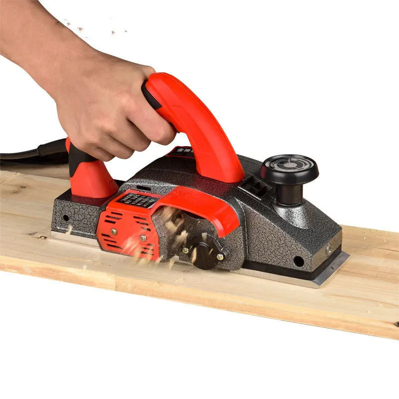 Red desktop electric wood planer with aluminium body on a workbench.