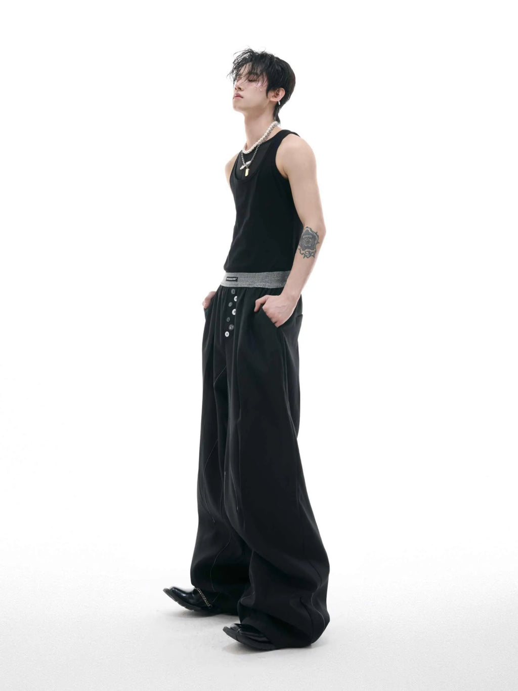 Men's black drooping straight-leg suit trousers with high waist and button detail.