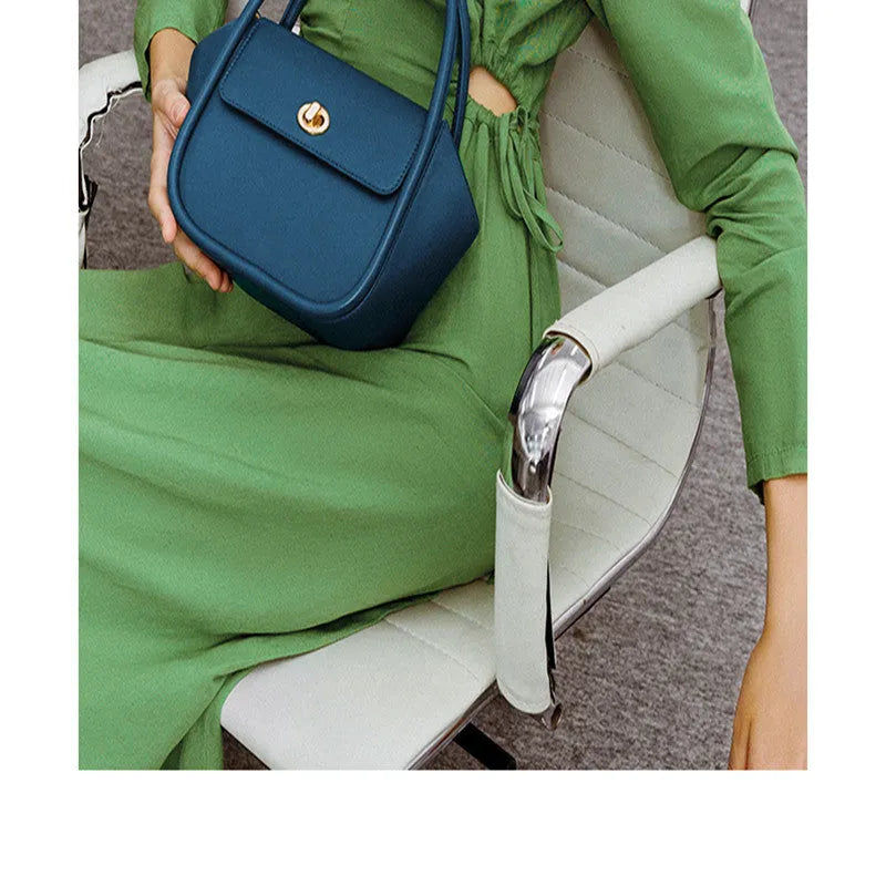 Women's wing-shaped leather tote bag with a latch buckle, shown in Atlantic blue with a cross-body strap.