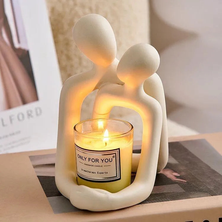 Modern resin sculpture of an embracing couple in milky white or gold finish on a wooden surface.