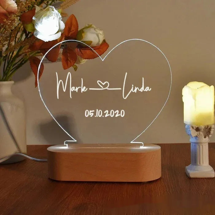 Custom transparent acrylic LED night light engraved with personal names and a date on a bedside table.