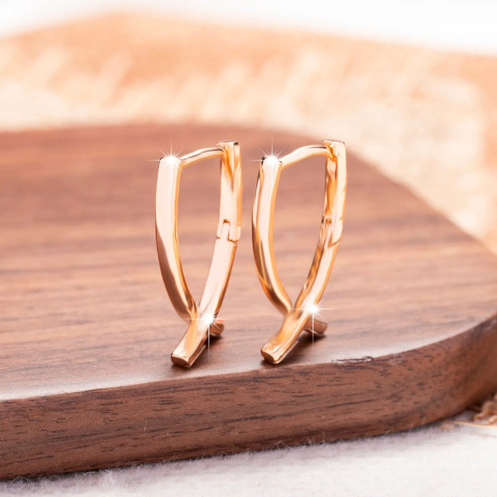A pair of rose gold coloured cross shaped earrings made from polished copper.