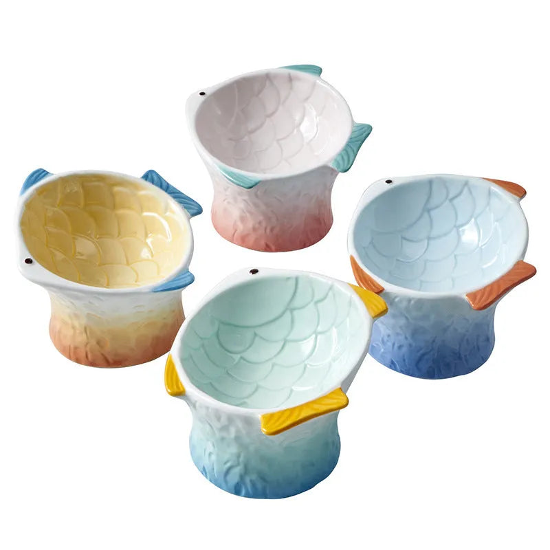 Set of four coloured fish-shaped ceramic cat bowls with elevated tilt design on a table.