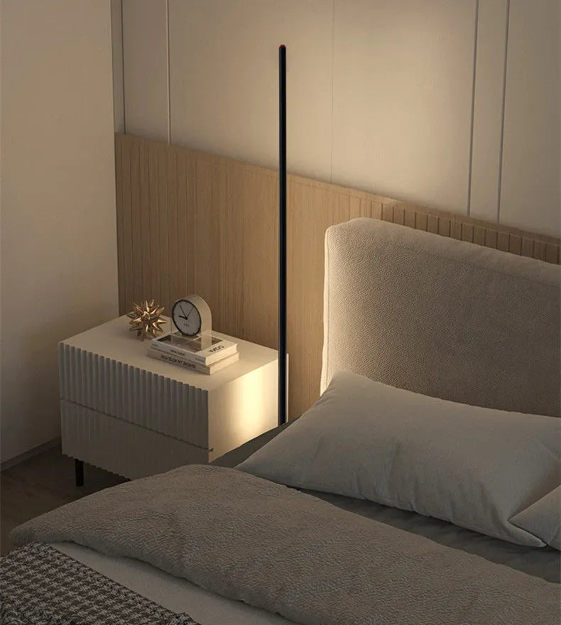 Modern vertical aluminium alloy floor lamp in silver, shown beside a sofa in a living room setting.