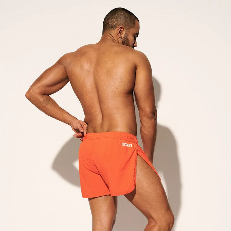 Man wearing loose orange polyester shorts on a beach, showcasing the elastic waist and fit for surfing.