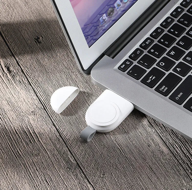 Portable white wireless charging dock for Apple Watch on a desk next to a laptop.