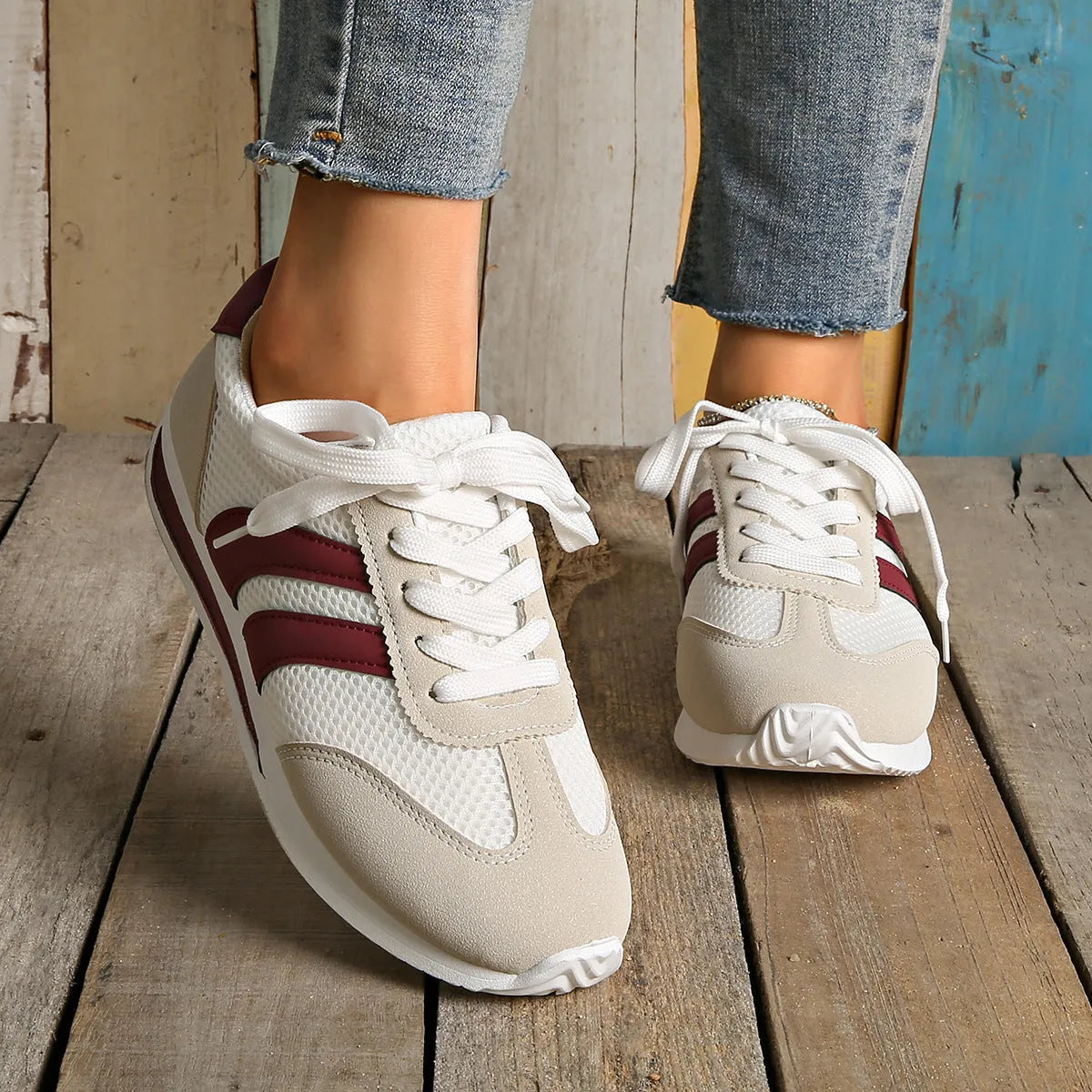 Wine red women's low-top sneaker with mesh upper, synthetic leather accents, and elastic cross straps on a flat rubber sole.