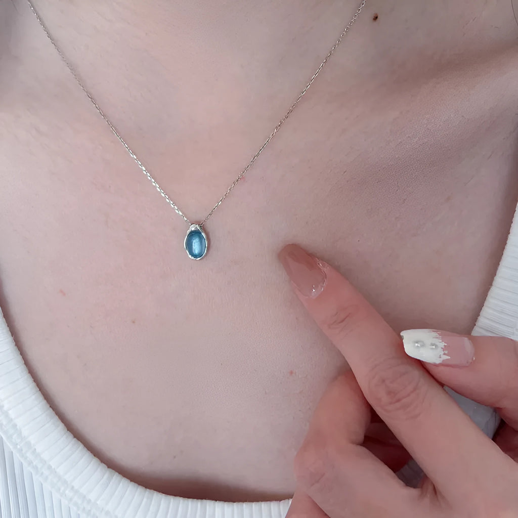 Close-up of a navy blue and platinum coloured geometric water drop pendant necklace on an adjustable copper chain.