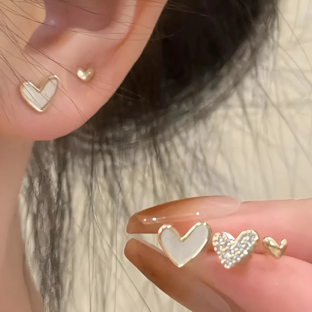 Three pairs of heart-shaped alloy earrings with love motif in gold, black, black and white, and pink colours.
