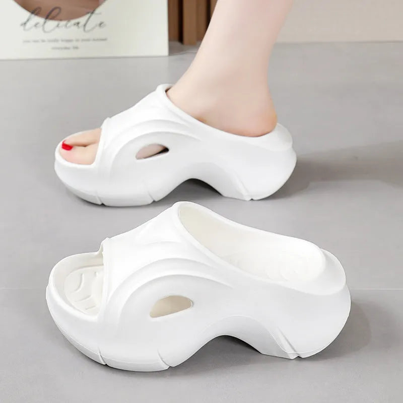 Women's white thick-soled EVA foam slippers with rounded toe on a beach.