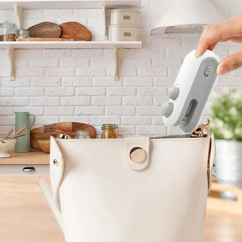 White and blue handheld USB rechargeable bag heat sealer with cutter blade on a kitchen counter.