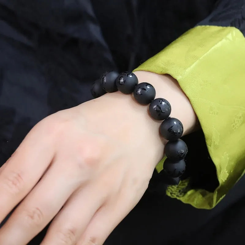 Close-up of a frosted black agate bracelet showing engraved Sanskrit mantra and Chinese-style patterns on a stone bead.