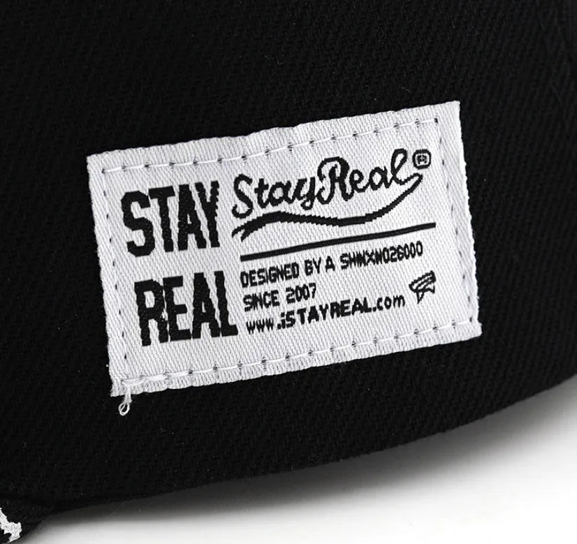 Black cotton baseball cap with white letter embroidery on the front, showing adjustable strap.
