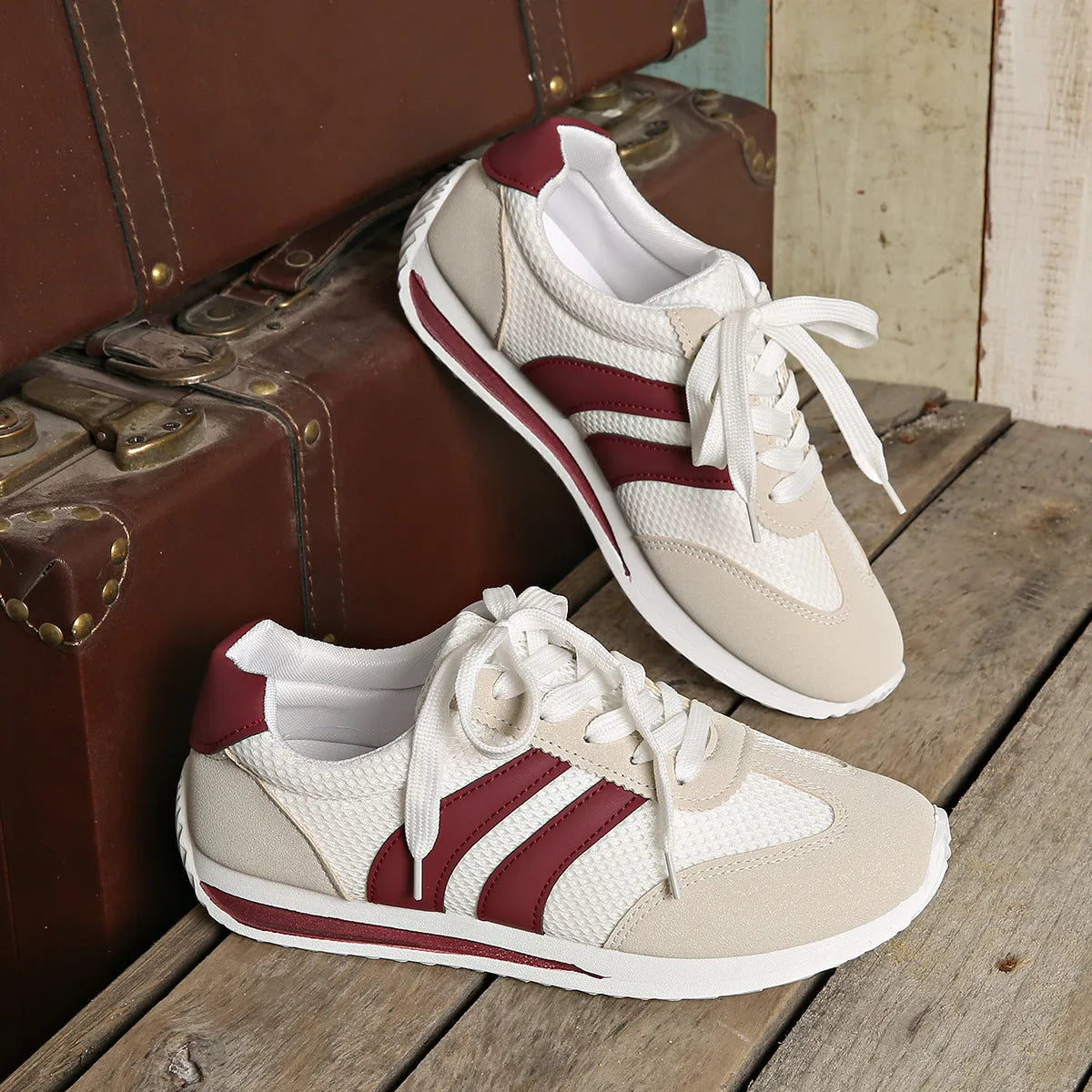 Wine red women's low-top sneaker with mesh upper, synthetic leather accents, and elastic cross straps on a flat rubber sole.