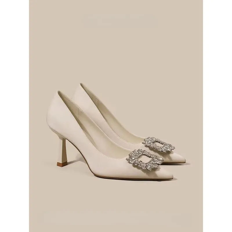 Creamy-white or black women's pointed toe high heels with a stiletto heel on a plain background.
