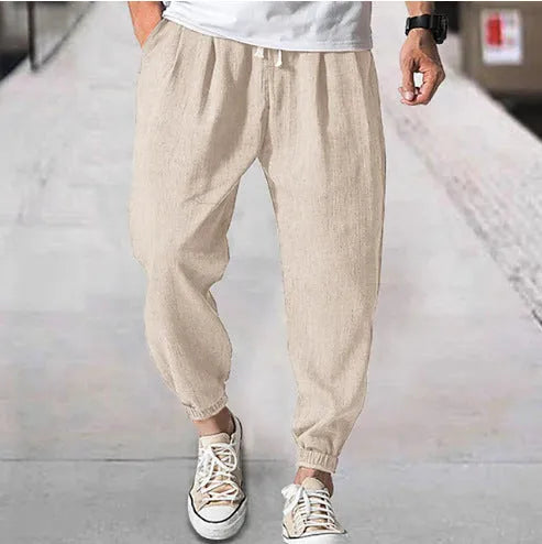 Men's loose fit cotton trousers with elasticated ankle bands in light green, shown in a casual summer setting.