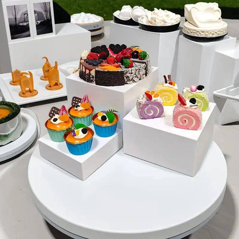 Set of six white plastic cubic dessert display stands in graduated sizes arranged in a row.