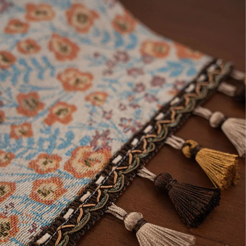 Beige jacquard table runner with long tassels and embroidered floral pattern.