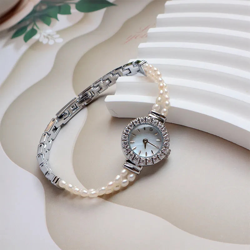 Women's light gold bracelet watch with freshwater pearls and a round 18mm dial on a stainless steel strap.