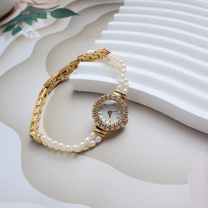 Women's light gold bracelet watch with freshwater pearls and a round 18mm dial on a stainless steel strap.