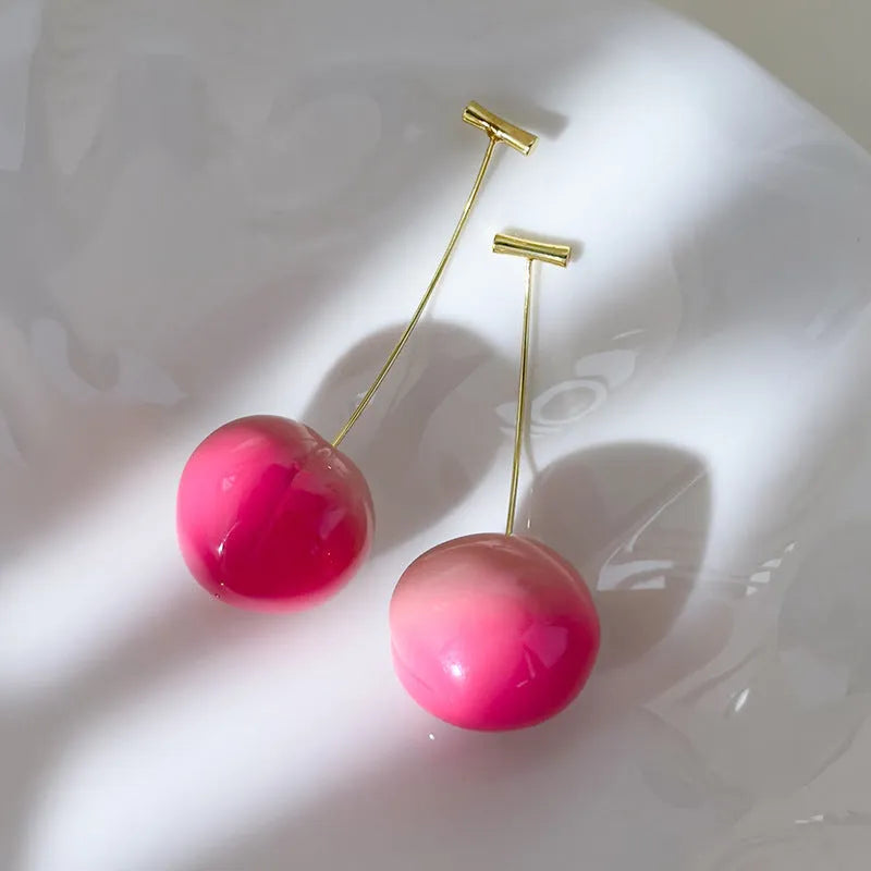 A pair of peach fruit-shaped stud earrings made from red and green acrylic with copper posts.