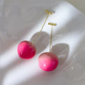 A pair of peach fruit-shaped stud earrings made from red and green acrylic with copper posts.
