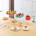 Set of six white plastic cubic dessert display stands in graduated sizes arranged in a row.