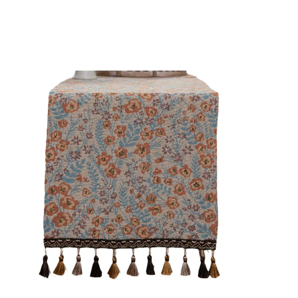 Beige jacquard table runner with long tassels and embroidered floral pattern.