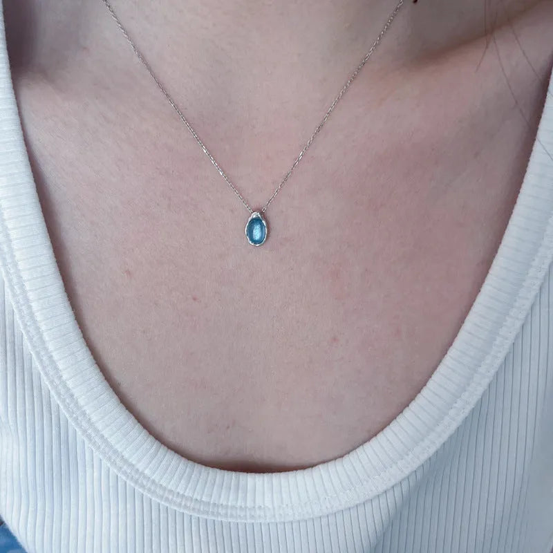 Close-up of a navy blue and platinum coloured geometric water drop pendant necklace on an adjustable copper chain.