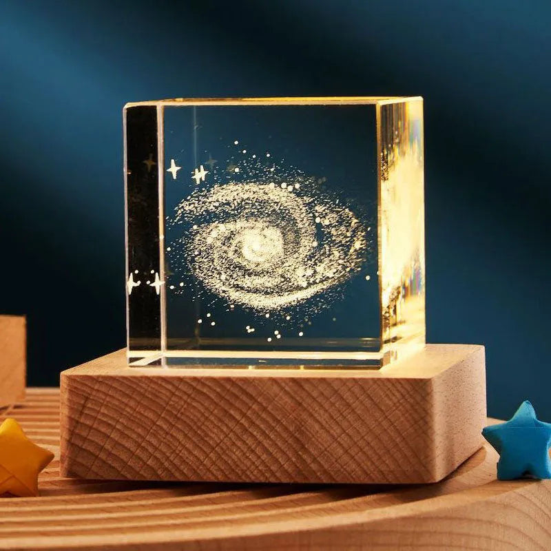 Transparent glass cube night lamp projecting a warm nebula light pattern on a desk.