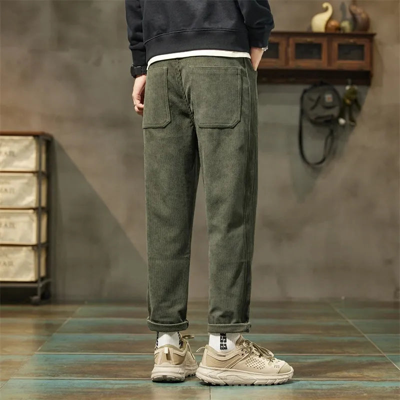 Man wearing tapered straight-leg corduroy trousers in army green, showing mid-rise waist and street style.