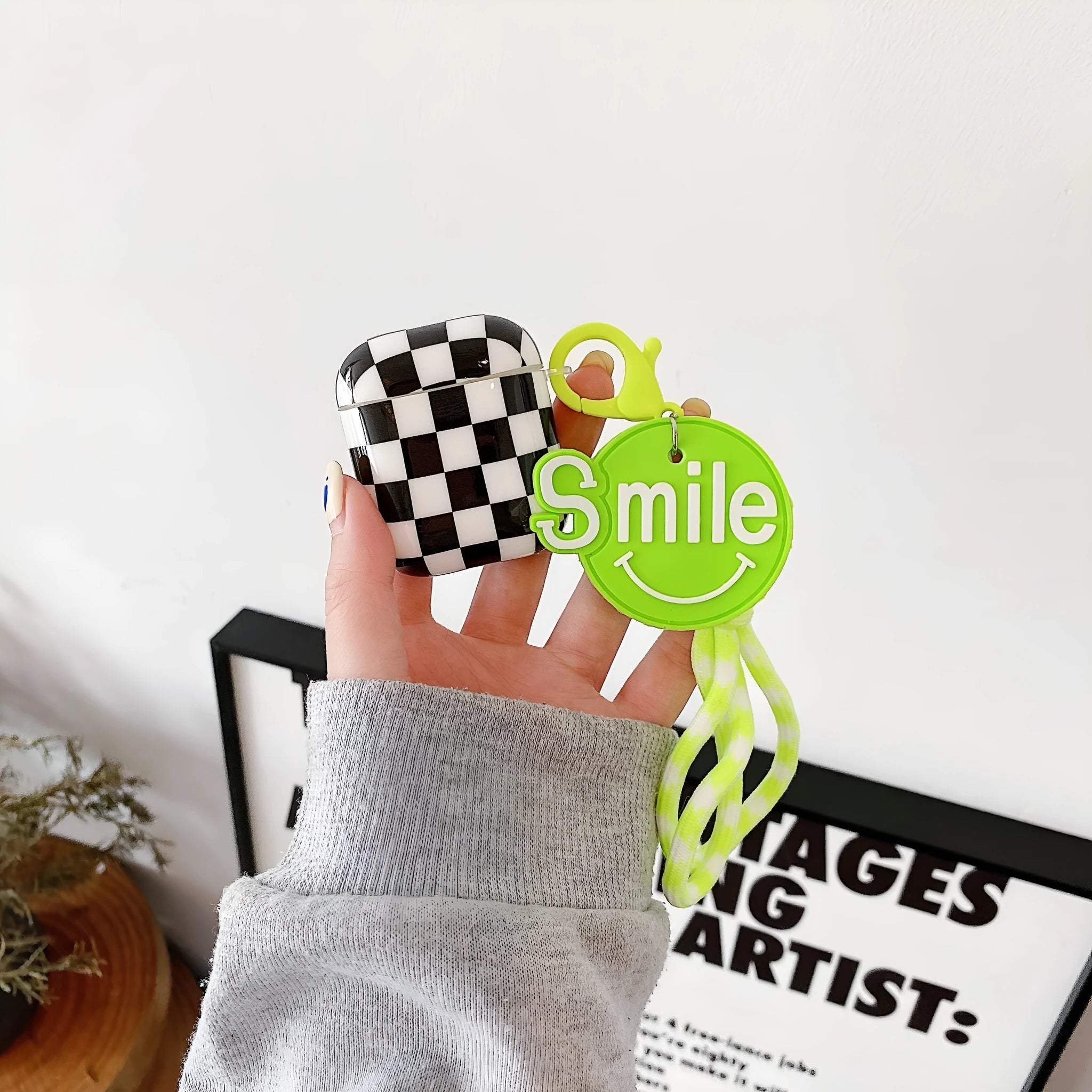 Black and green checkerboard pattern TPU protective case covers for Apple AirPods, one with a smiley face lanyard.