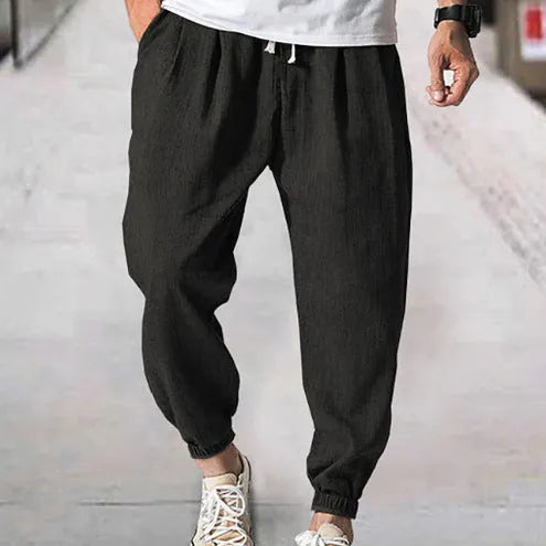 Men's loose fit cotton trousers with elasticated ankle bands in light green, shown in a casual summer setting.